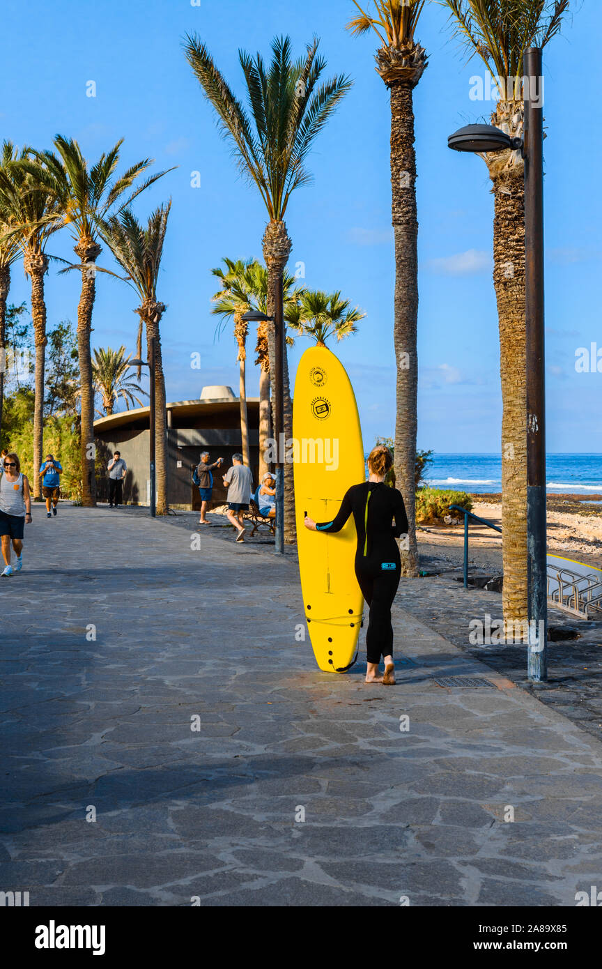 Beautiful Caucasian Blond Girl With Back Leaning On Her Yellow Board Waiting On The Promenade Her Surf Class On The Beach Of The Americas. April 11, 2 Stock Photo