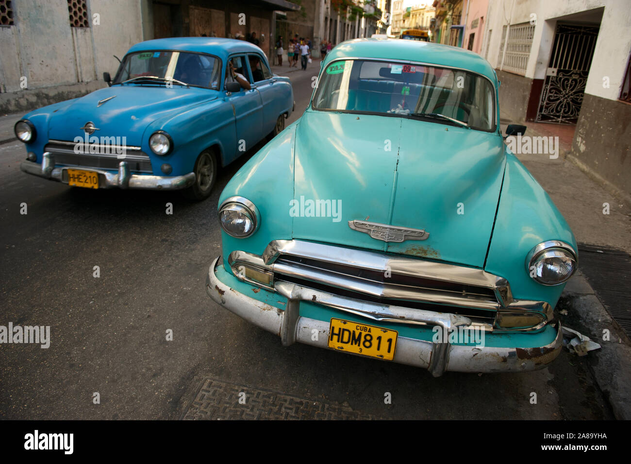 HAVANA - MAY 16, 2011: A classic car passes another parked on a street in Centro. Vintage American cars from the 1950s are found all over Cuba. Stock Photo