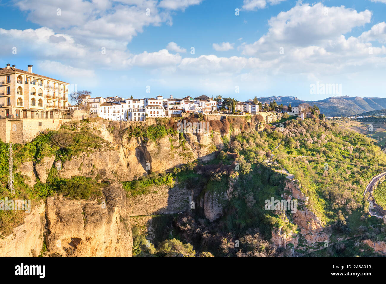 Ronda, Spain: Landscape of white houses on the green edges of steep cliffs with mountains in the background. Stock Photo