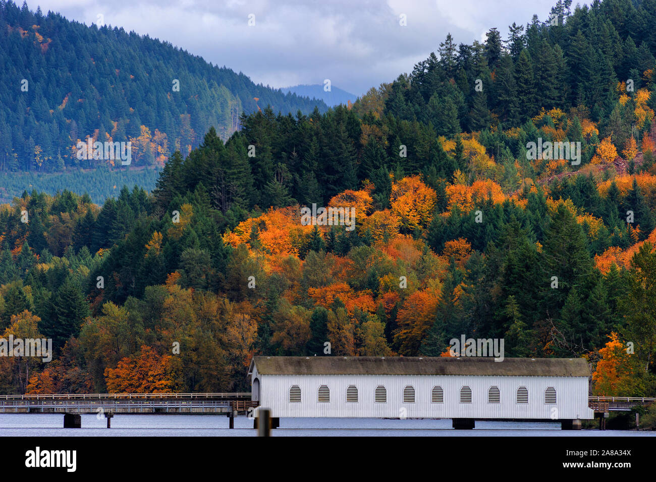 Autumn colors in the Cascade Mountain Range, where a covered bridge sits along the shore of a lake Stock Photo