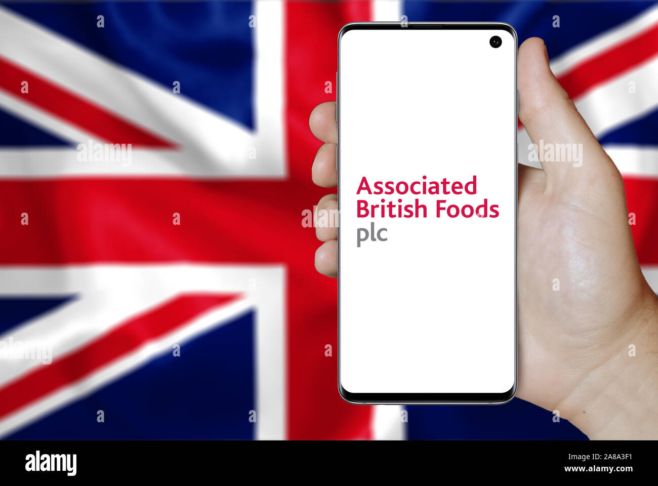 Logo of public company Associated British Foods displayed on a smartphone. Flag of UK background. Credit: PIXDUCE Stock Photo