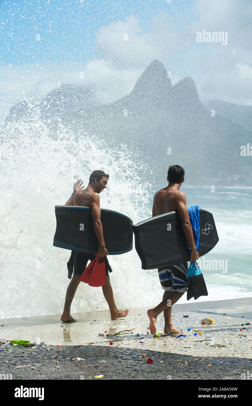 RIO DE JANEIRO - MARCH 16, 2011: Young Brazilian surfers walk on the Ipanema boardwalk carrying bodyboards and fins near crashing waves at Arpoador. Stock Photo