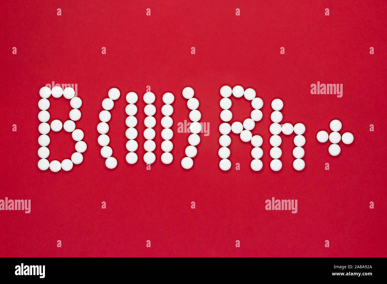 Third blood type. Blood type symbol from white pills on a red background. Blood type treatment