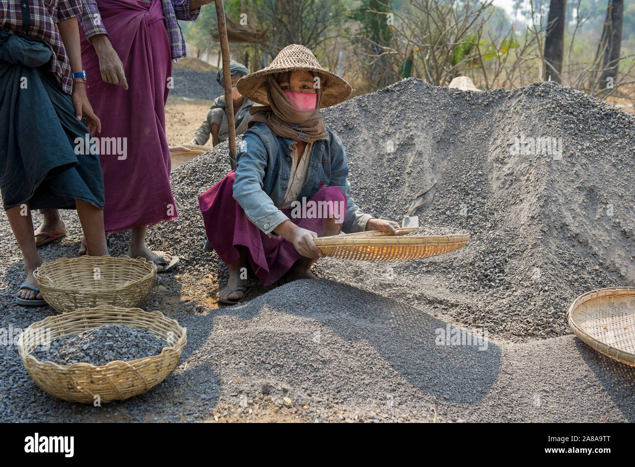 Women in traditional clothing sorting stones with woven baskets at a road construction site in rural Myanmar, Burma Stock Photo