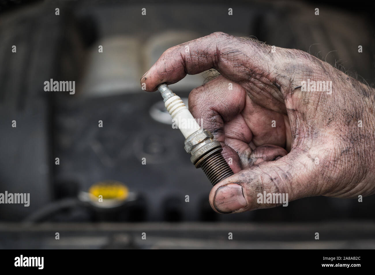 Auto mechanic holding spark plug in front of vehicle engine. Stock Photo