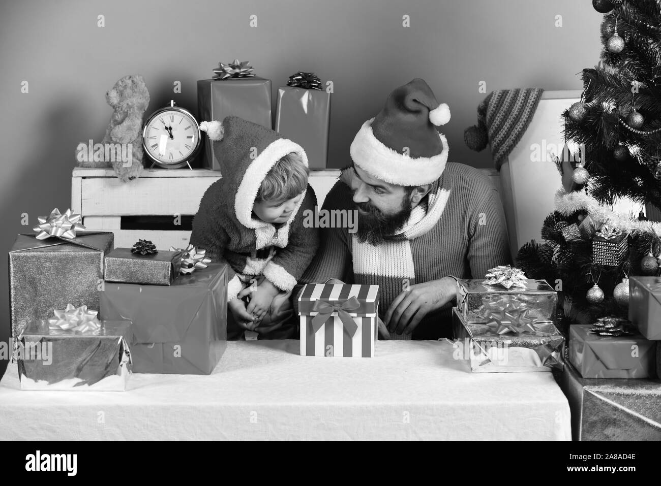 Man with beard and boy with shocked faces look at box. Christmas family opens presents on blue background. Boxing day and family concept. Santa and little assistant among gift boxes by Christmas tree Stock Photo