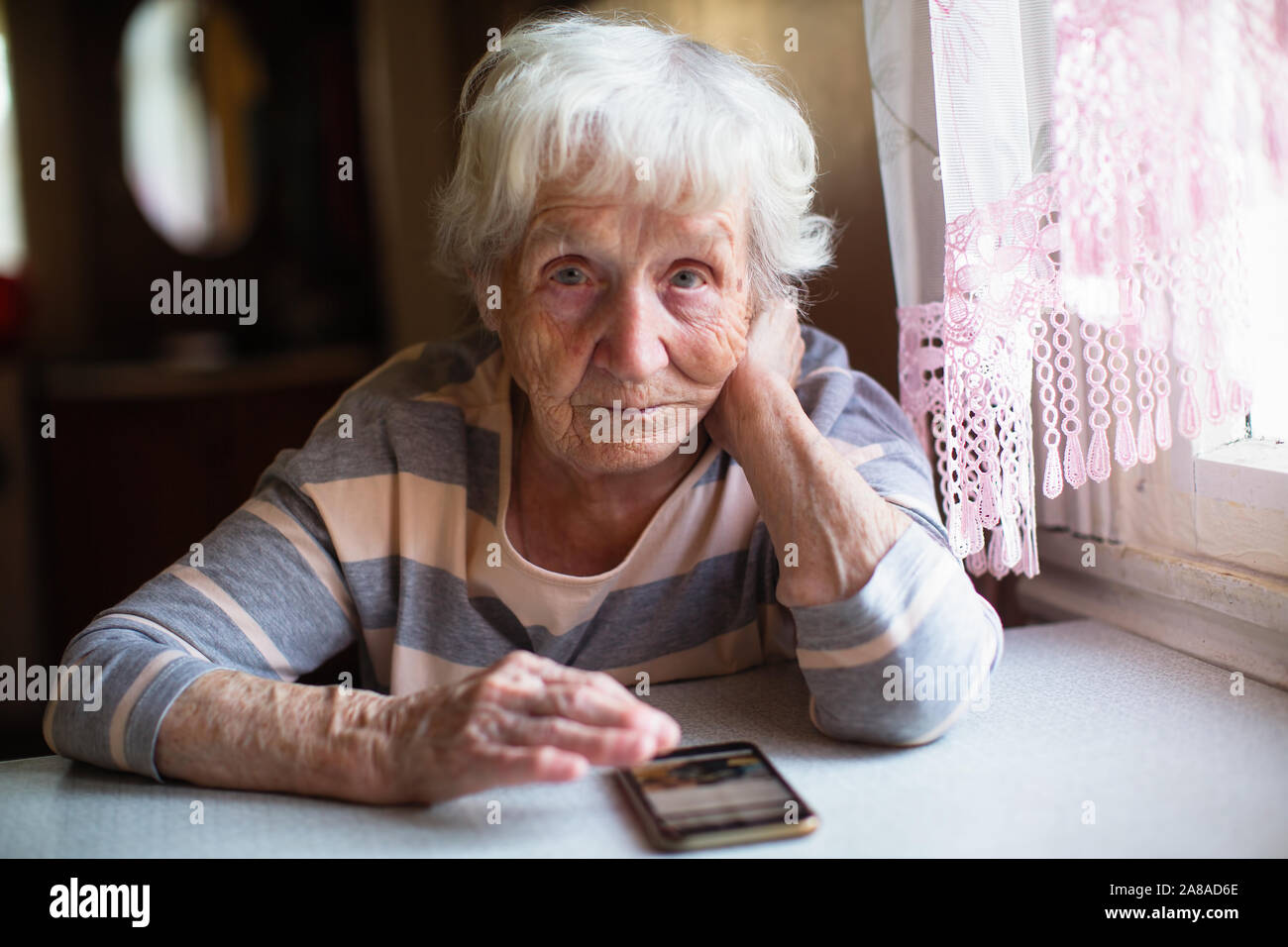 Elderly woman sits with smartphone at the table. Stock Photo