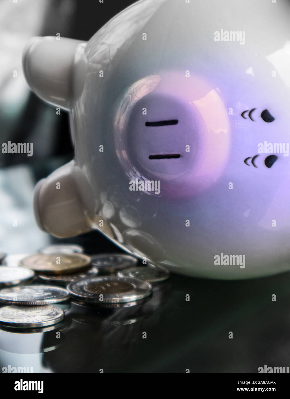 Sad and very tired piggy bank is lying on the side, next to few coins. Stock Photo
