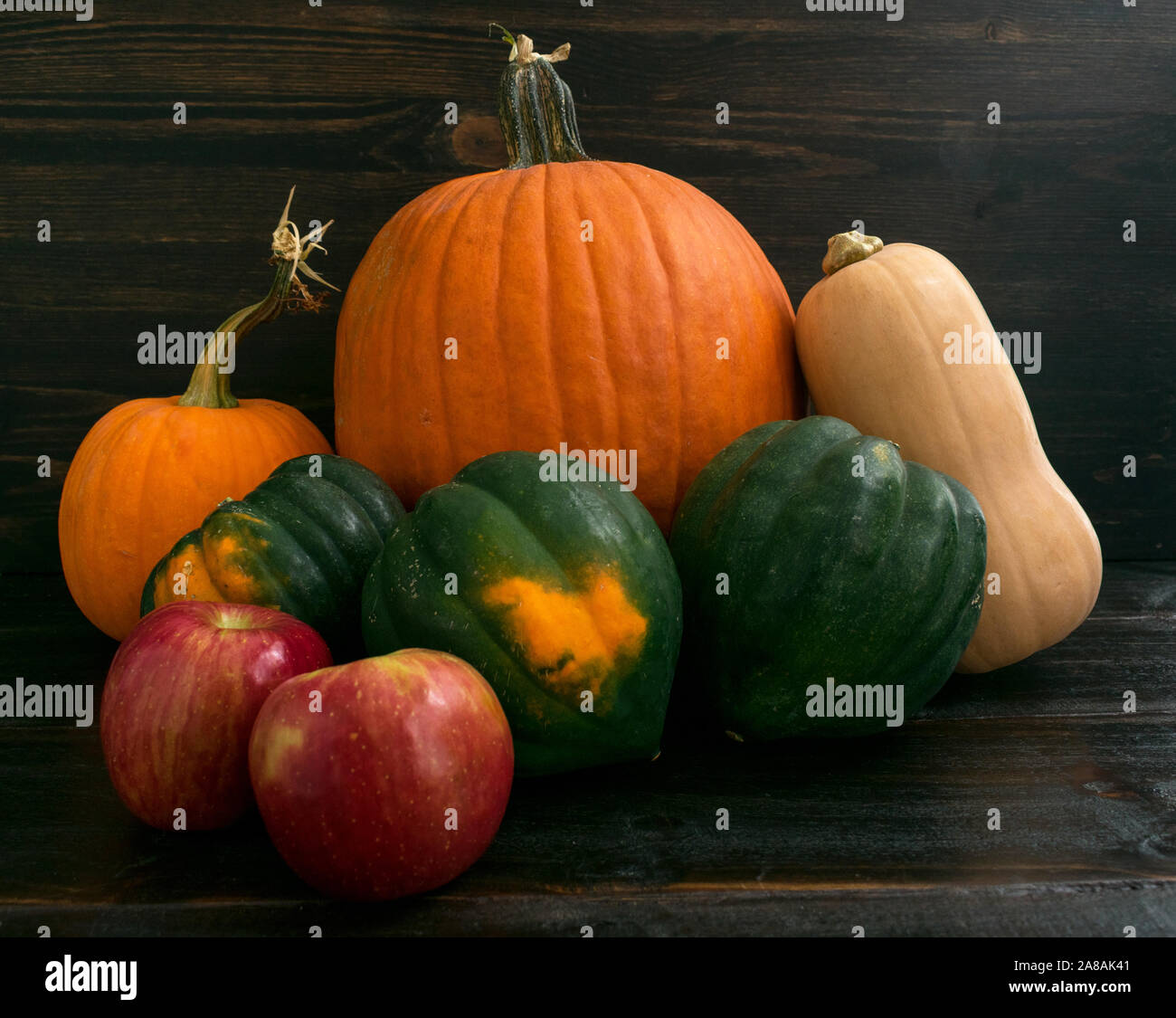 Rustic grouping of apples, acorn squash, butternut squash, and pumpkins on a dark wood background Stock Photo