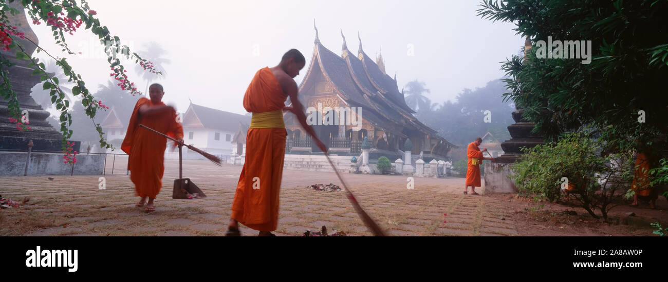 Buddhist monks sweeping temple courtyard, Vat Xieng Thong, Luang Prabang, Laos Stock Photo