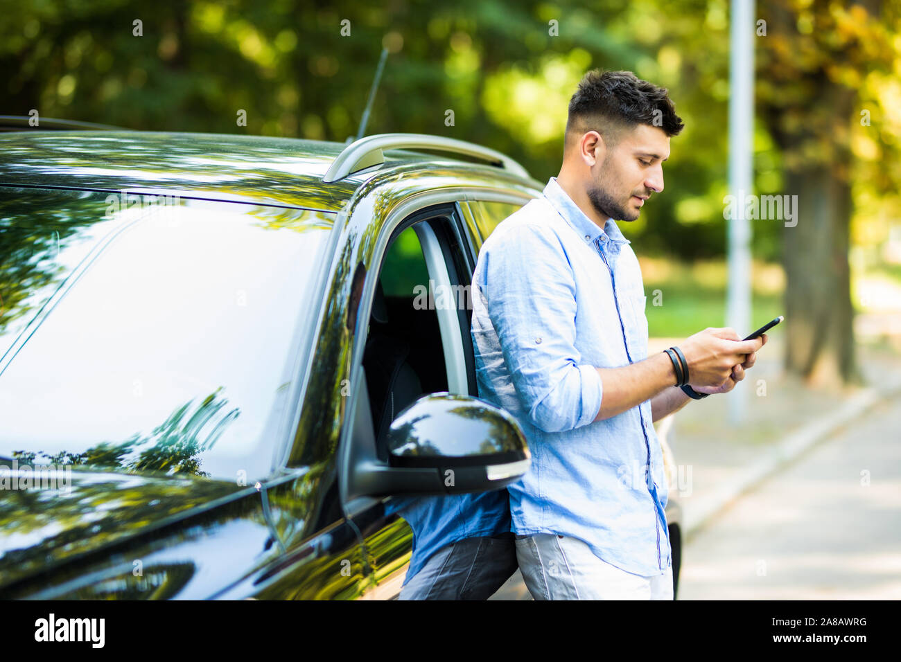 Handsome man standing and using the phone with his car. Stock Photo