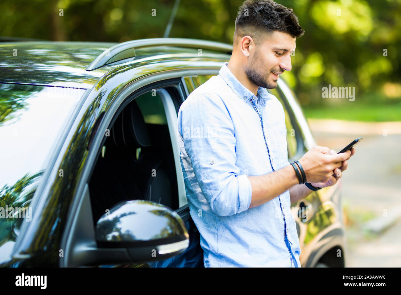 Handsome man standing and using the phone with his car. Stock Photo