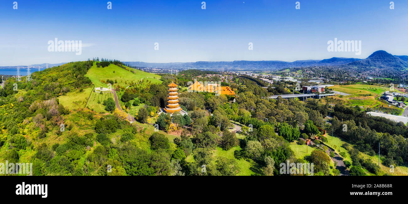 Green hillside of Australia with asian Bhuddist temple Nan Tien near Wollongong with leafy public park and tall multi-level pagoda in wide aerial pano Stock Photo