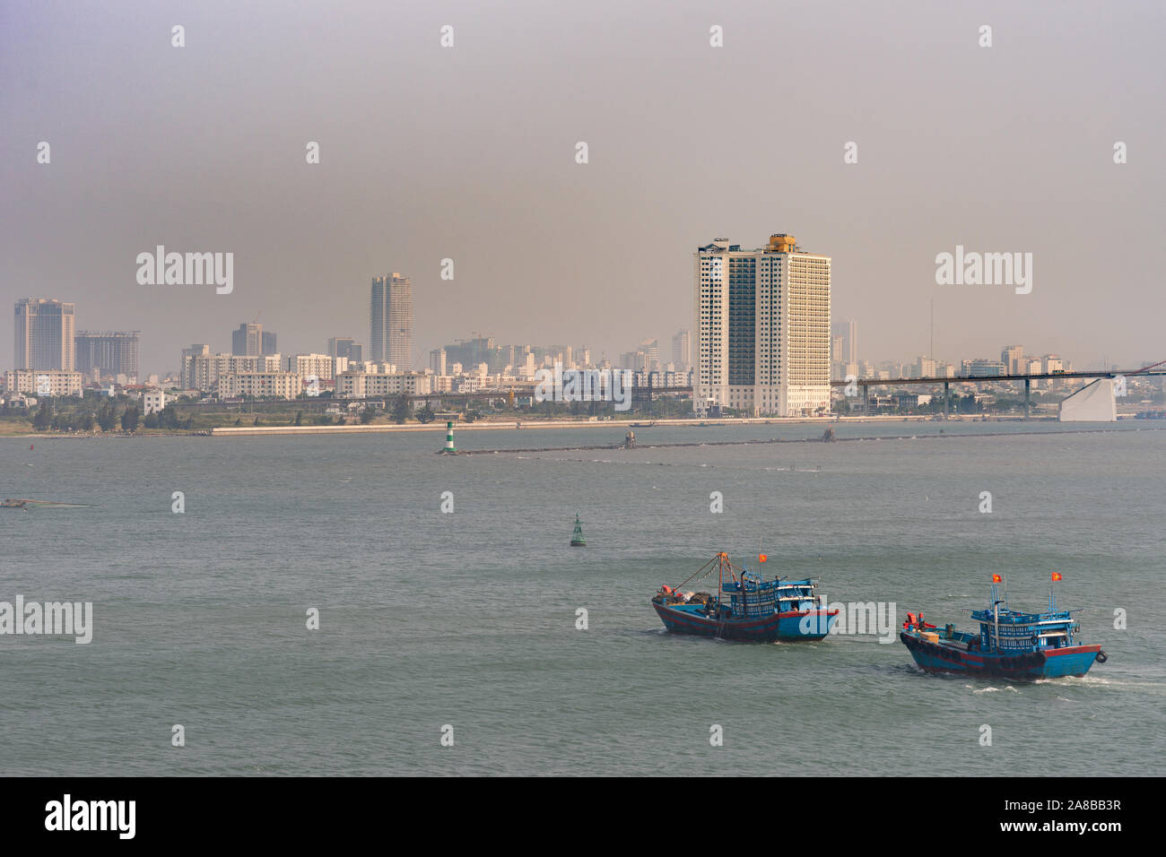 Da Nang, Vietnam - March 10, 2019: Tien Sa Port in Da Nang Bay. 2 blue and red fishing vessels return home in evening. Cityscape and long on ramp of T Stock Photo