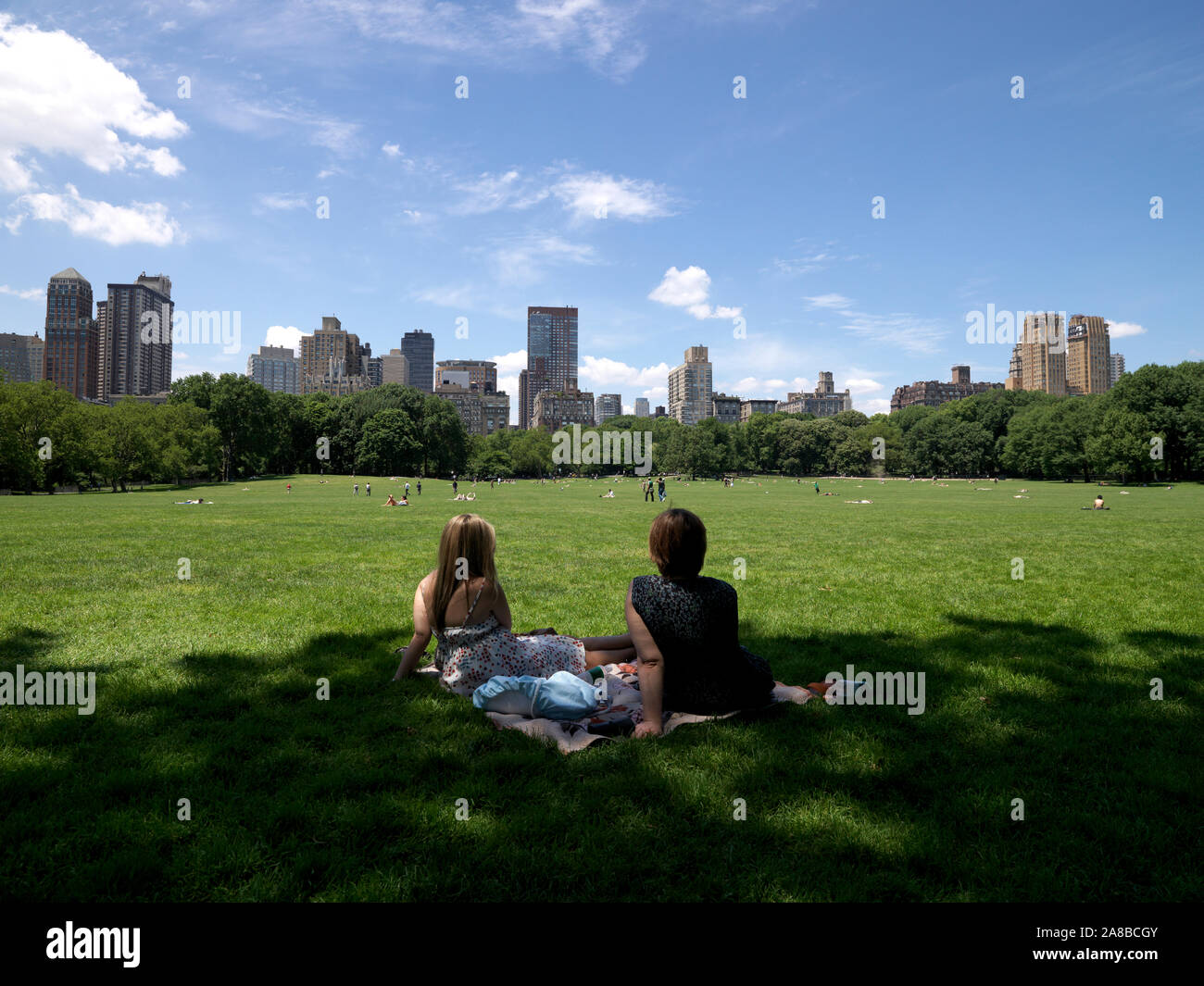 Two young women sitting on the east sid of Sheep Meadow, south end of Central Park, Manhattan, New York City, New York State, USA Stock Photo