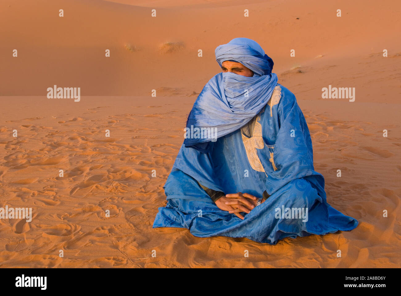 Veiled Tuareg man sitting on sand, Erg Chebbi, Morocco Stock Photo