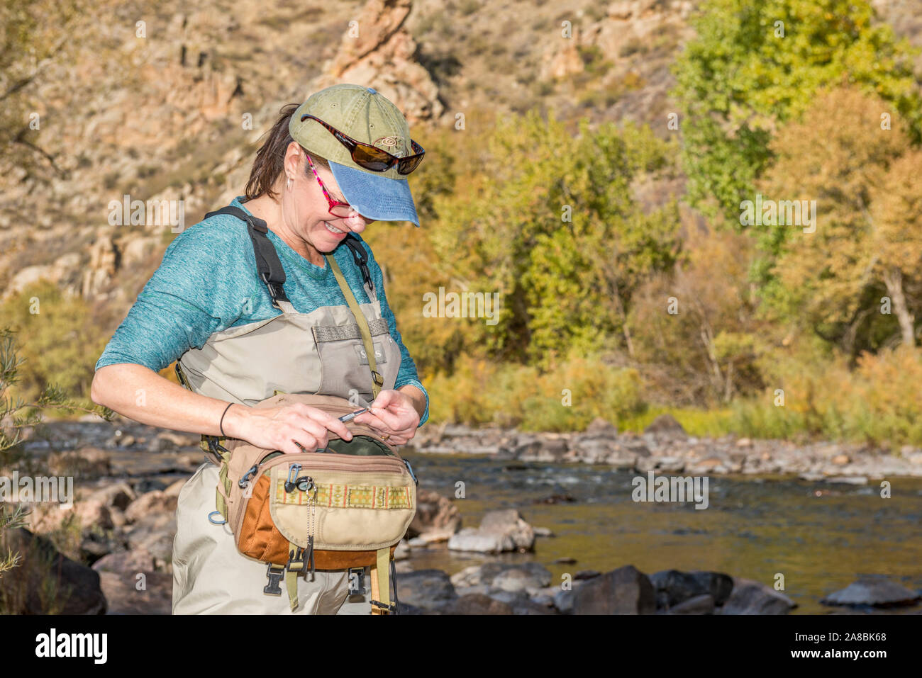 A woman prepares her fishing pole with line and a hook as she heads onto the Poudre River for an afternoon of fishing. Stock Photo