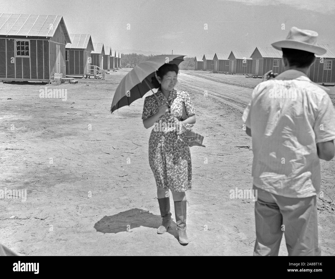 Poston, Arizona. This evacuee is fortified with an umbrella for protection from the sun, and high- top boots for strolling through the dusty streets at this War Relocation Authority center 5/9/1942 Stock Photo
