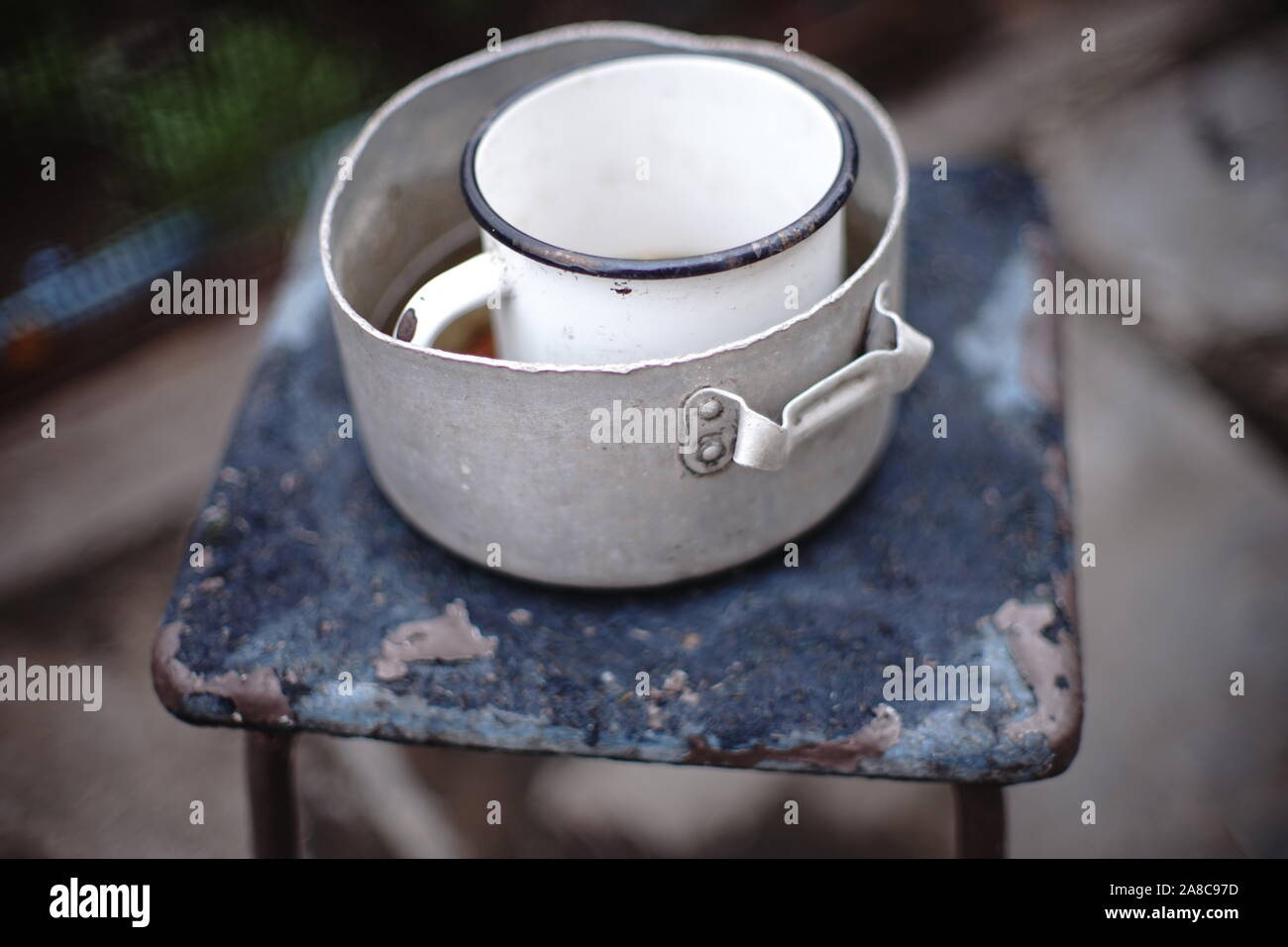 Old crockery on a retro stool. Aluminum pan and enameled mug on a chair