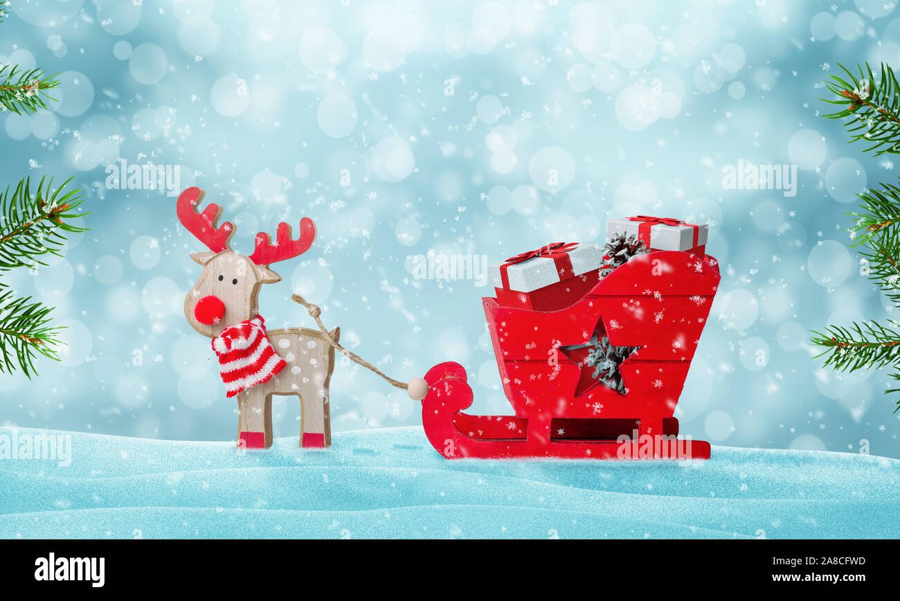 Santa's sleigh full of gifts in snow. Deer pulls the sled. Cute wooden toy. Christmas tree beside. Copy space above. Stock Photo