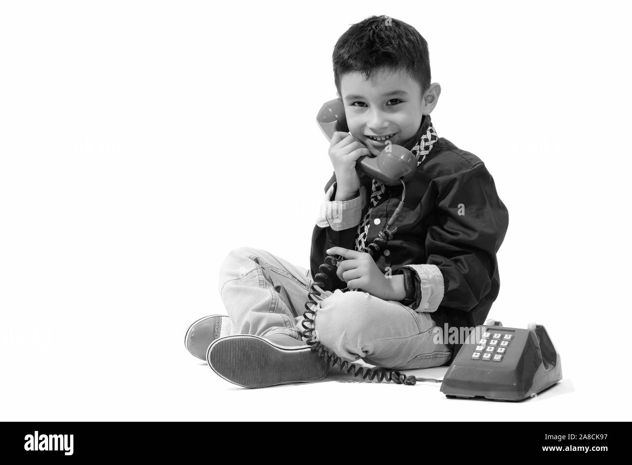 Studio shot of cute happy boy smiling and talking on old telephone Stock Photo
