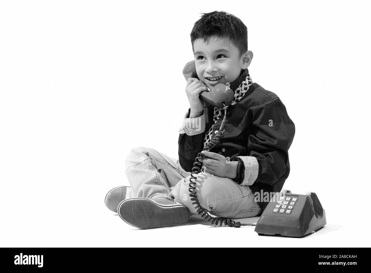 Studio shot of cute happy boy smiling and talking on old telephone while thinking Stock Photo