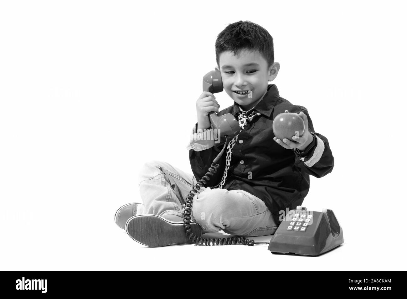 Studio shot of cute happy boy smiling and talking on old telephone while holding green apple Stock Photo