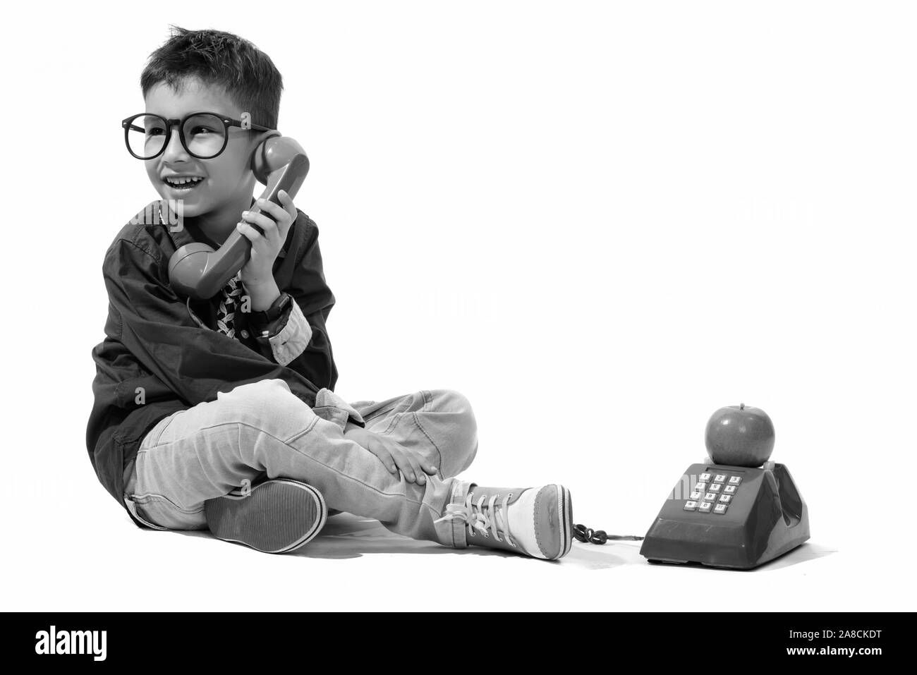 Studio shot of cute happy boy smiling and talking on old telephone while looking away Stock Photo