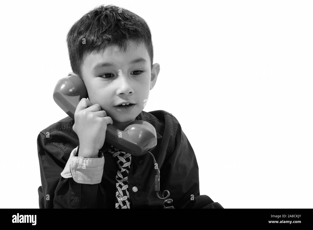 Studio shot of cute boy talking on old telephone and looking down Stock Photo