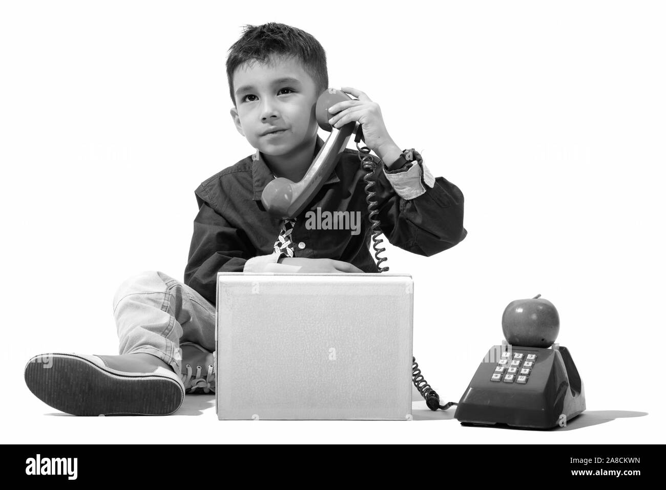 Studio shot of cute boy talking on old telephone while thinking Stock Photo