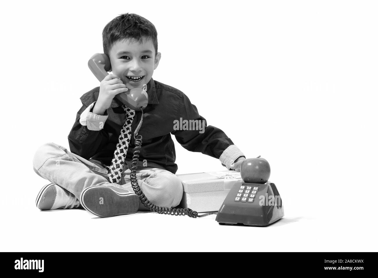 Studio shot of cute happy boy smiling while talking on old telephone and holding gift box Stock Photo