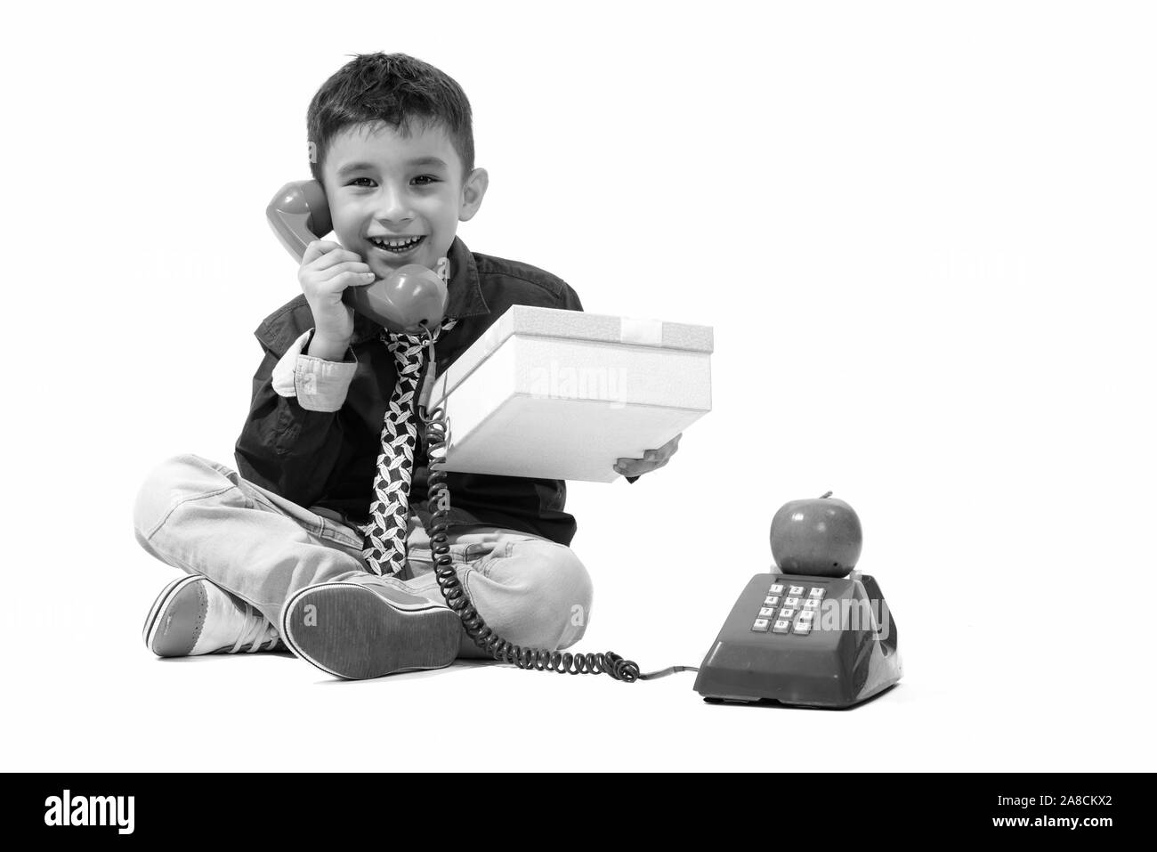 Studio shot of cute happy boy smiling while talking on old telephone and giving gift box Stock Photo