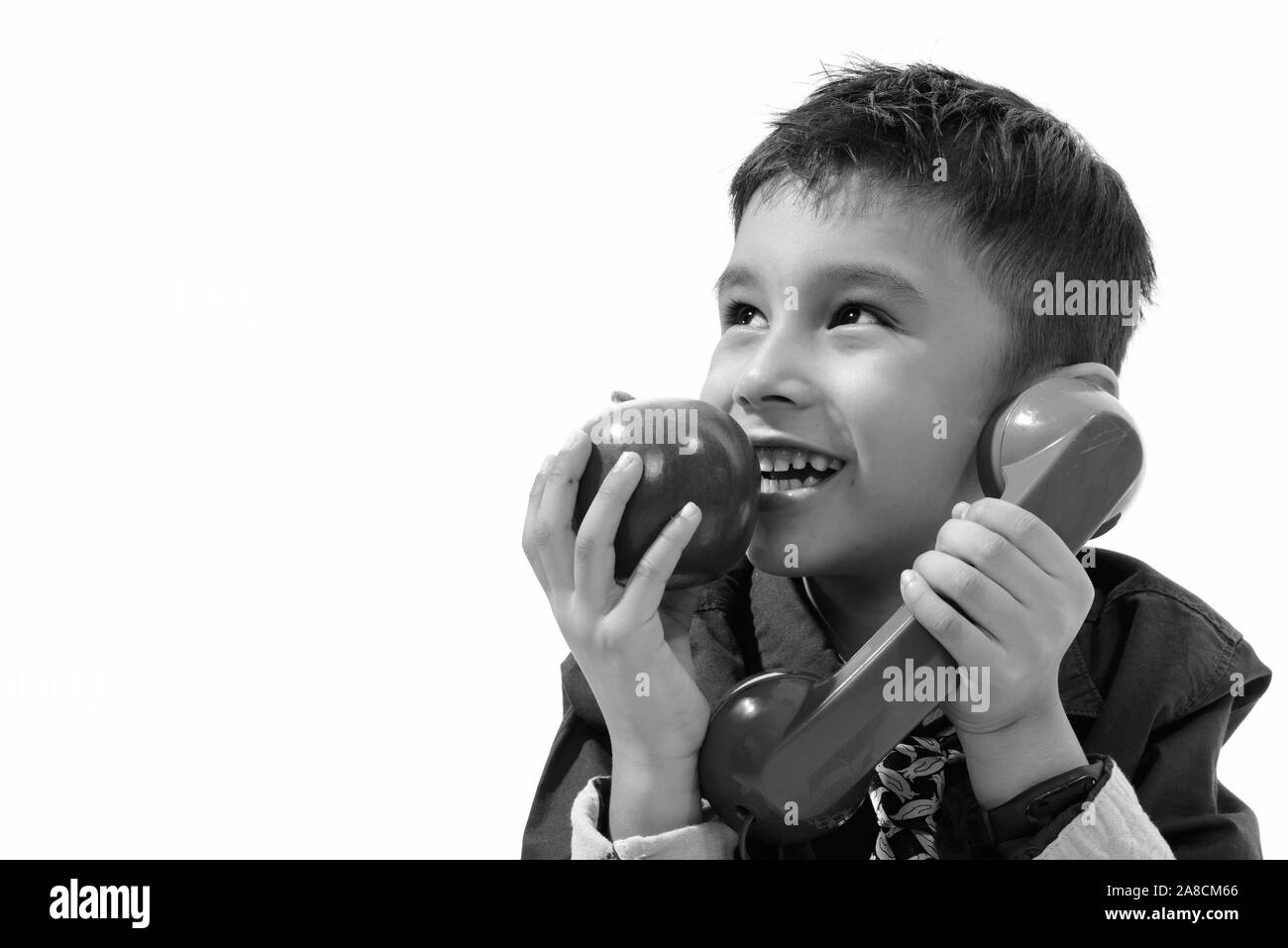 Thoughtful cute happy boy smiling while talking on old telephone and eating apple Stock Photo