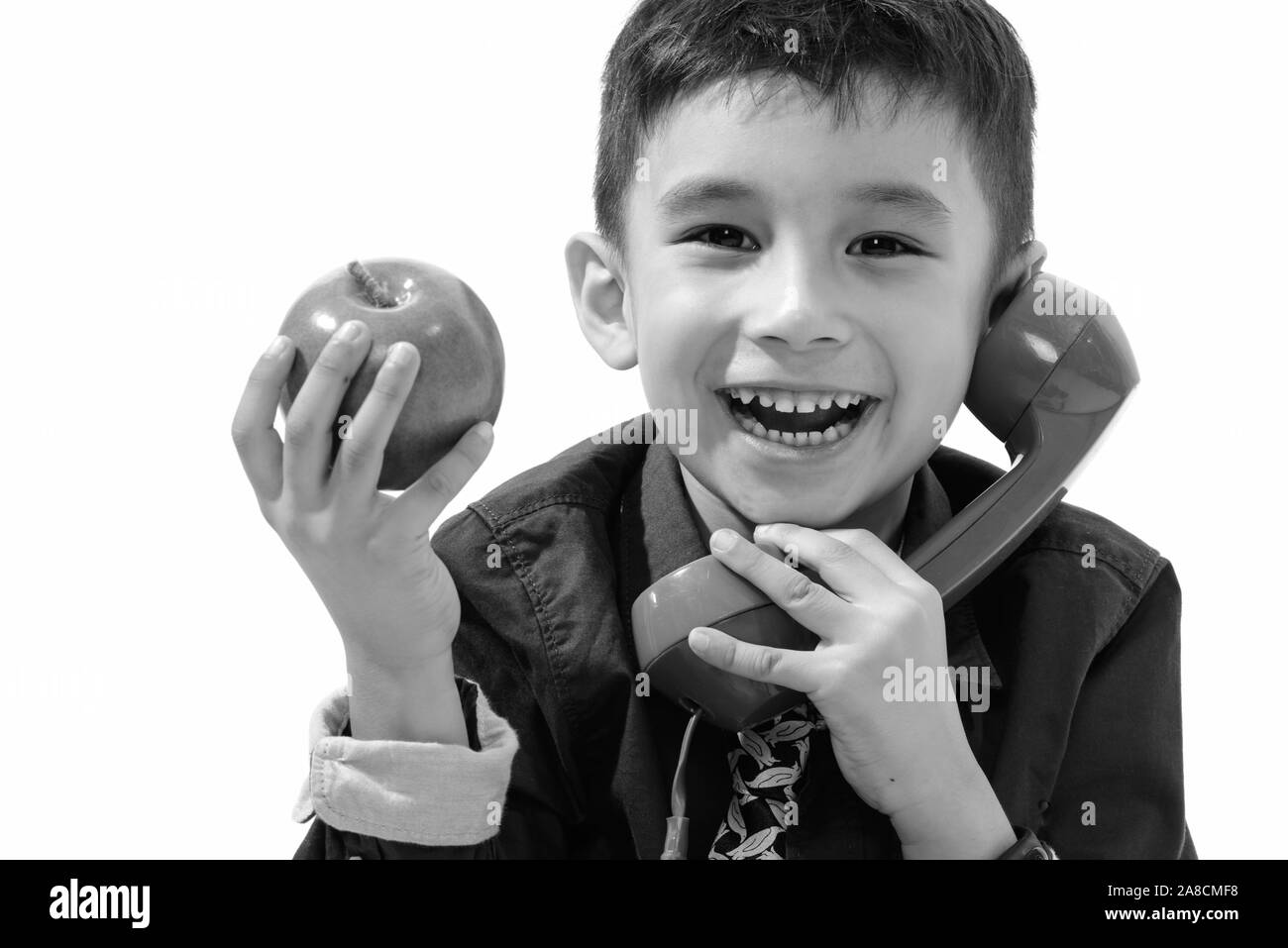 Studio shot of cute happy boy smiling and holding green apple while talking on old telephone Stock Photo