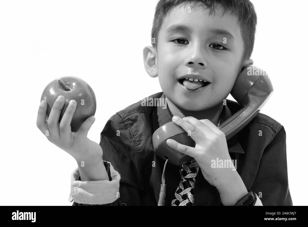 Cute boy sticking tongue out while holding green apple and talking on old telephone Stock Photo