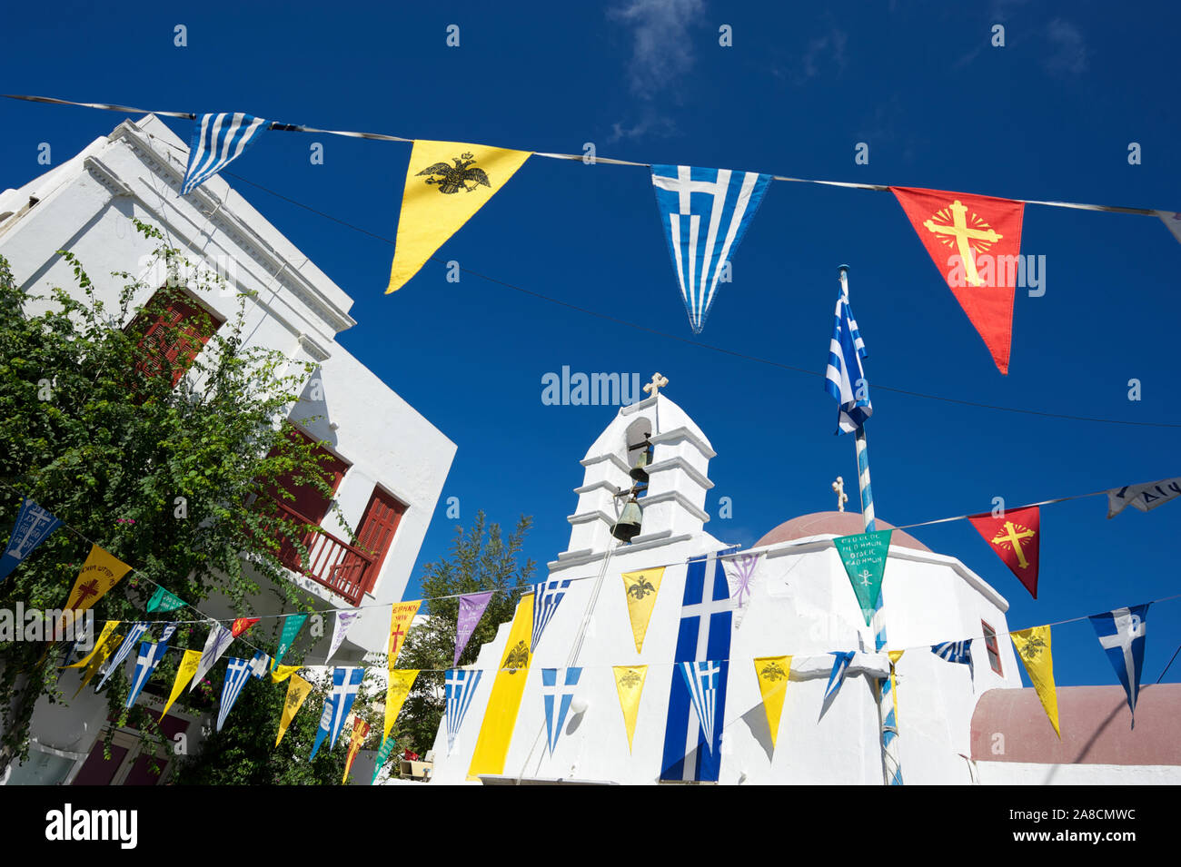 Bright sunny view of plaza decorated with pennant flag bunting representing Greece, the Byzantine Empire, and the Greek Orthodox Church in Mykonos Stock Photo