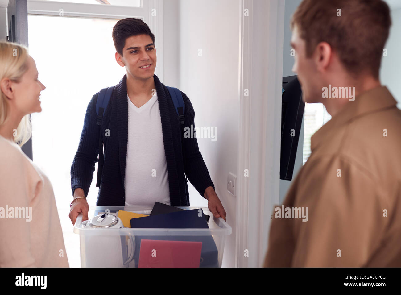 Male College Student Carrying Box Moving Into Accommodation Meeting House Mates Stock Photo