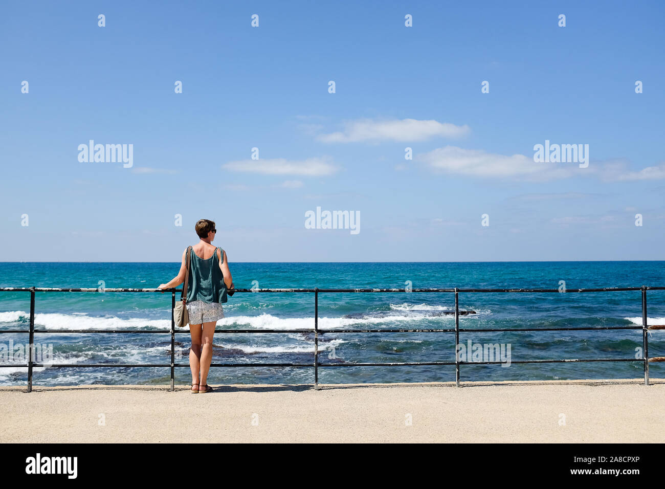 Woman looking out over the sea with blue sky Stock Photo