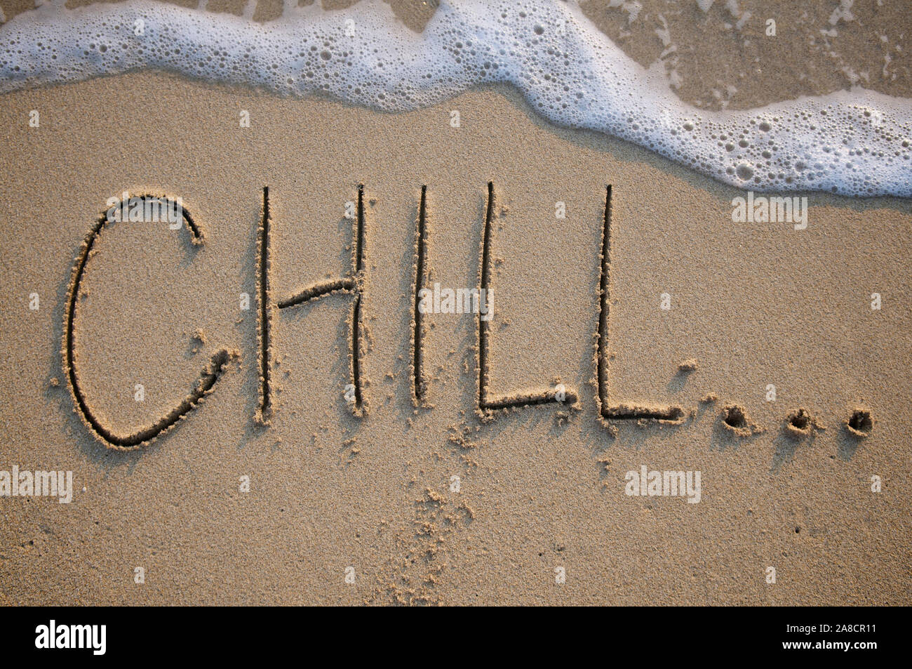 Chill... message handwritten on smooth sand beach with incoming wave ...