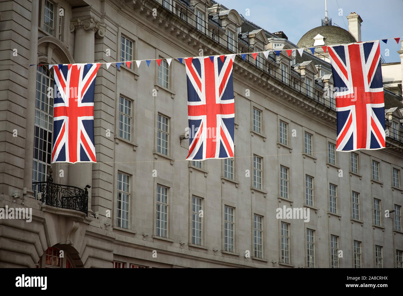 Union Jack flag decorations strung above the streets of London, UK under soft blue sky Stock Photo