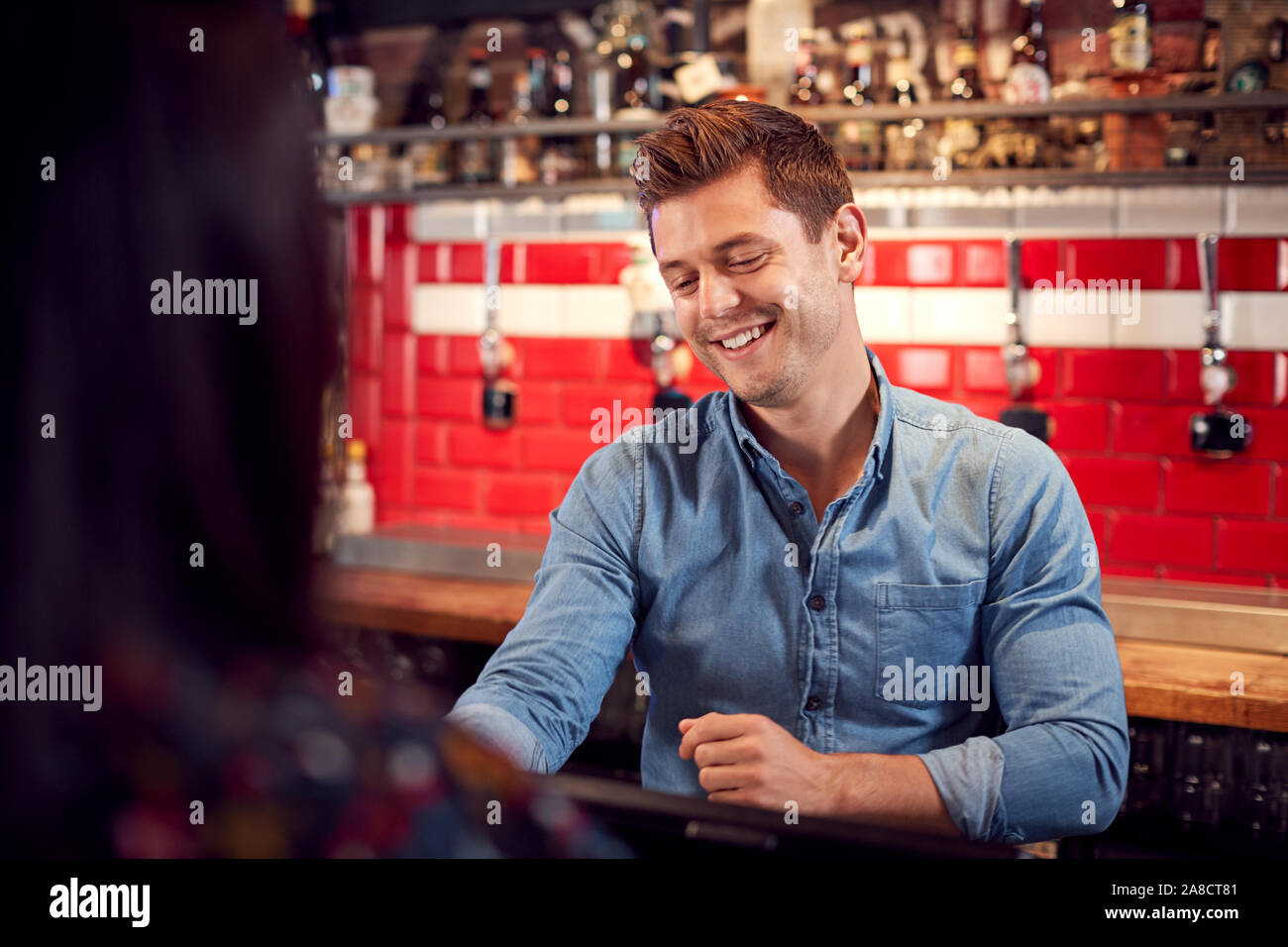 Male Bar Tender Standing Behind Counter Serving Drinks To Customer