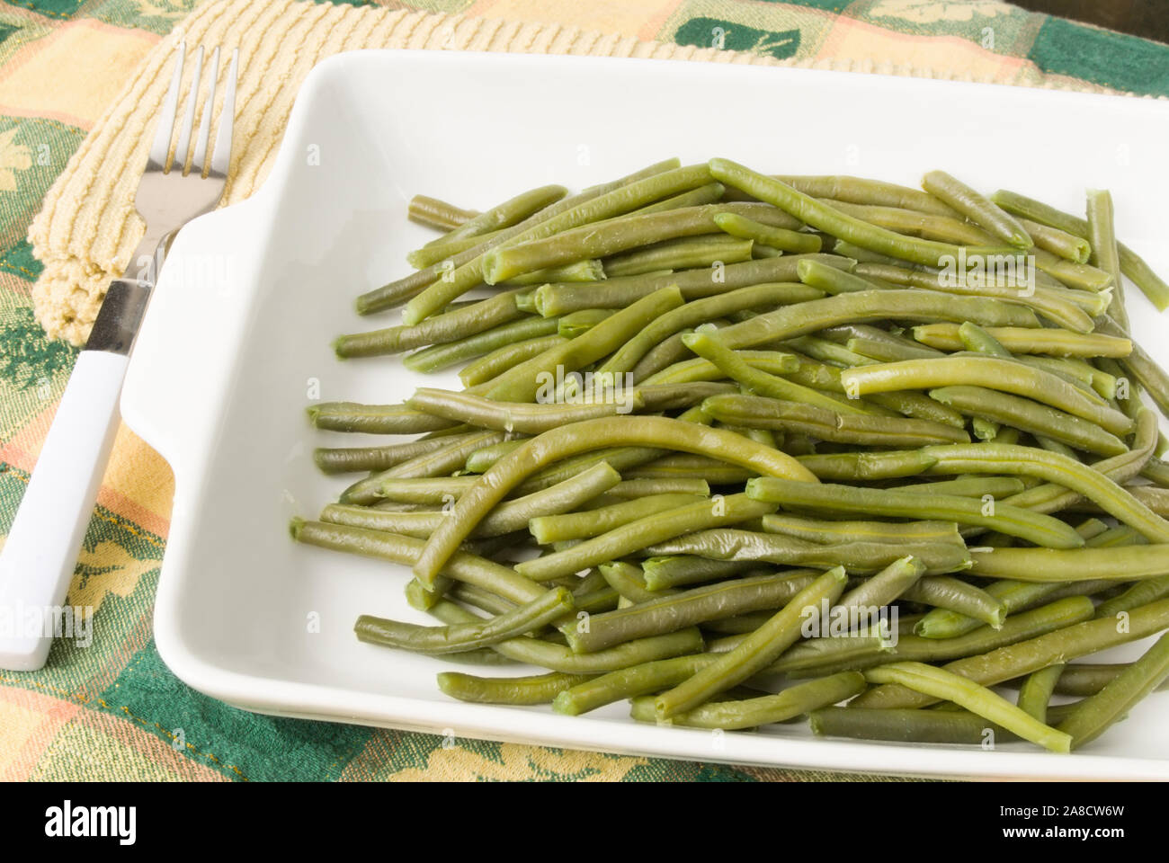 homemade cooked string green beans served in a white casserole dish on a Thanksgiving holiday themed tablecloth. Stock Photo