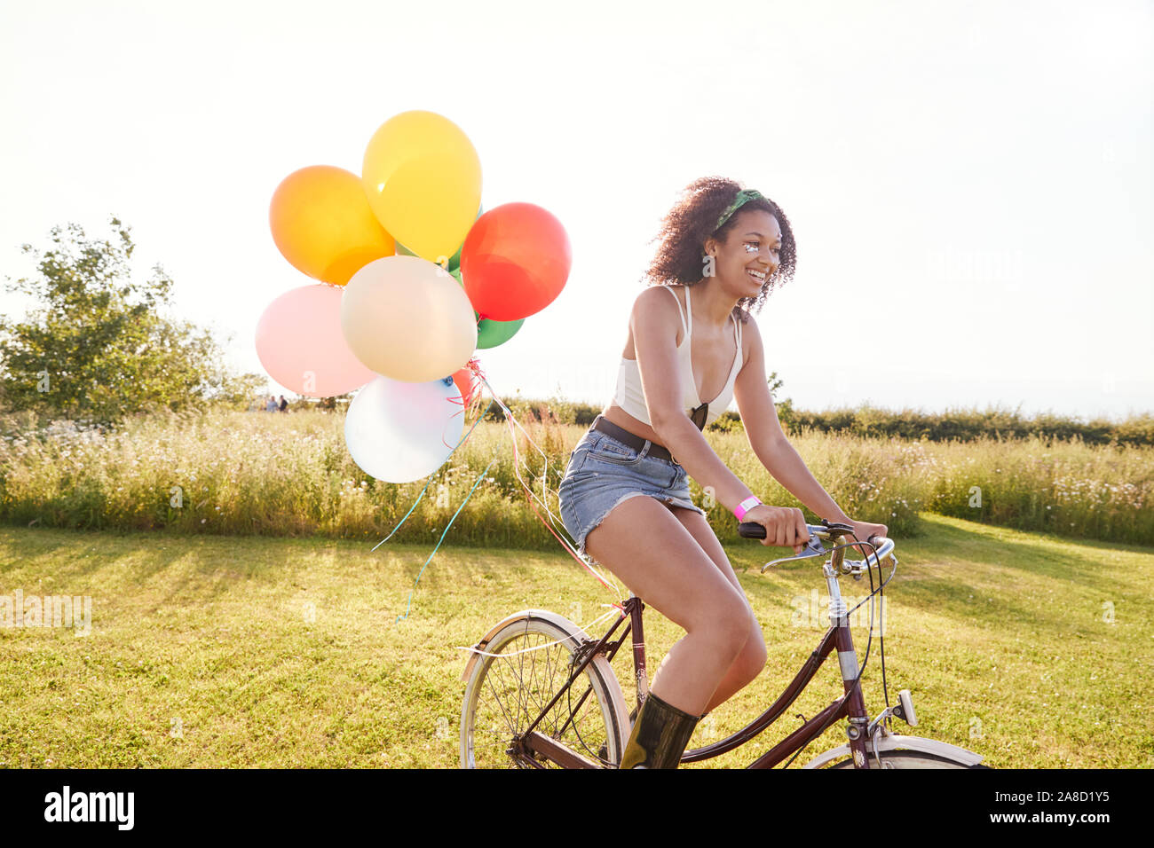 Young Woman Riding Bicycle Decorated With Balloons Through