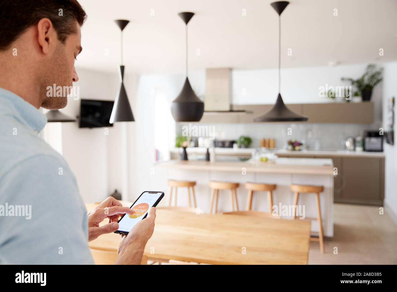 Man Using App On Smart Phone To Control Central Heating Temperature In House Stock Photo