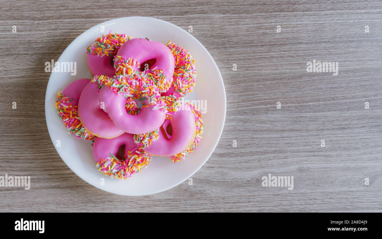 Pink glazed mini donuts in white plate on wooden table. Sweet food background Stock Photo
