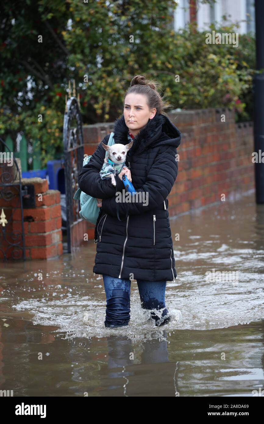A woman carries her dog six through floodwater in Doncaster, Yorkshire, as parts of England endured a month's worth of rain in 24 hours, with scores of people rescued or forced to evacuate their homes, others stranded overnight in a shopping centre, and travel plans thrown into chaos. Stock Photo