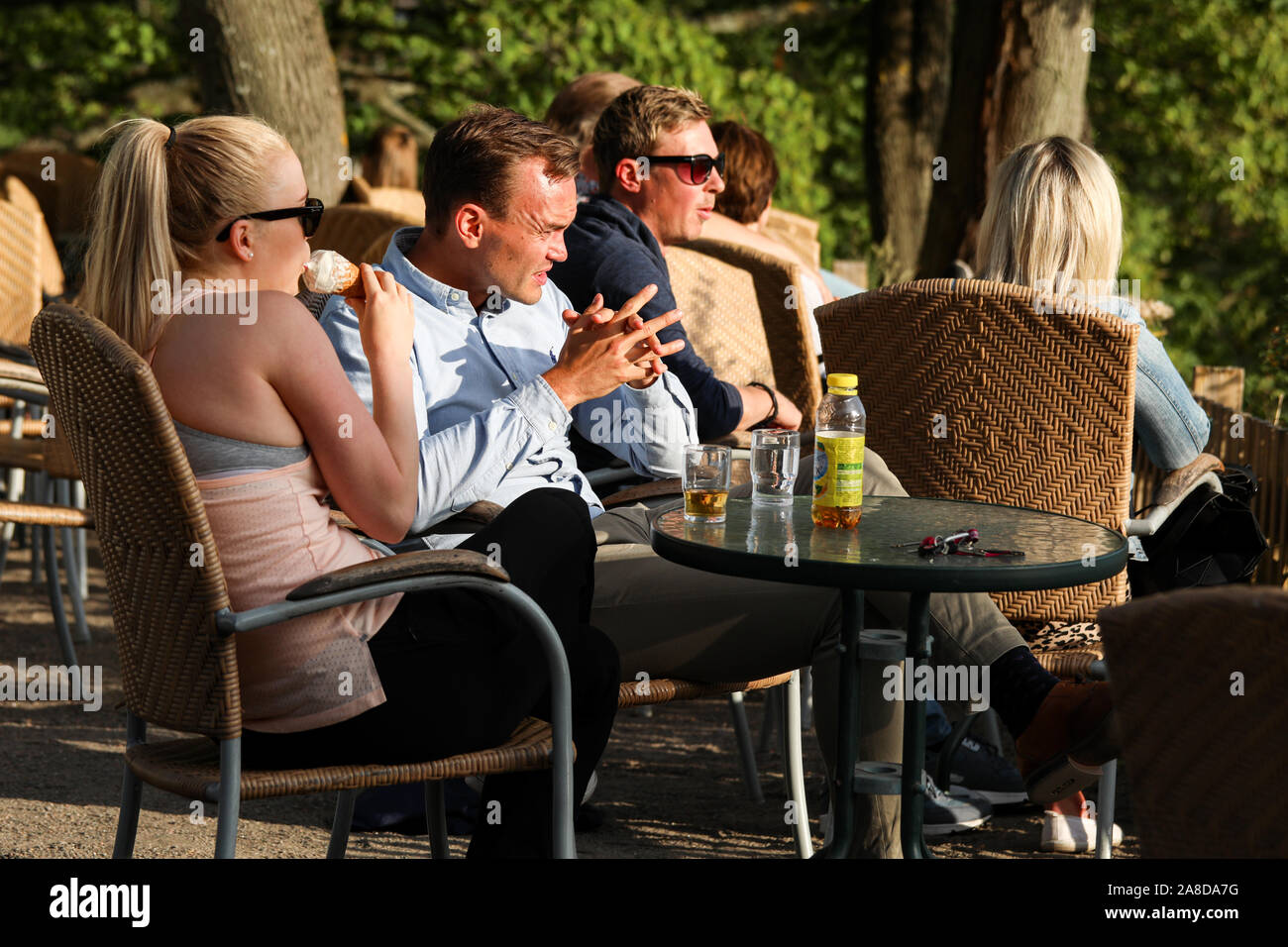 People basking in evening sun enjoying beverages at open-air cafe Stock Photo