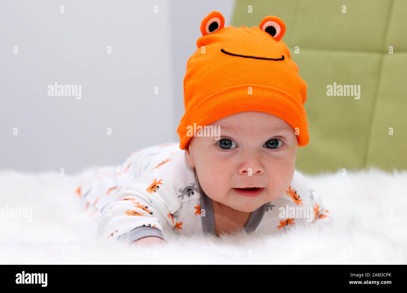 The charming Baby in an orange hat lies on a stomach on white fur Stock Photo