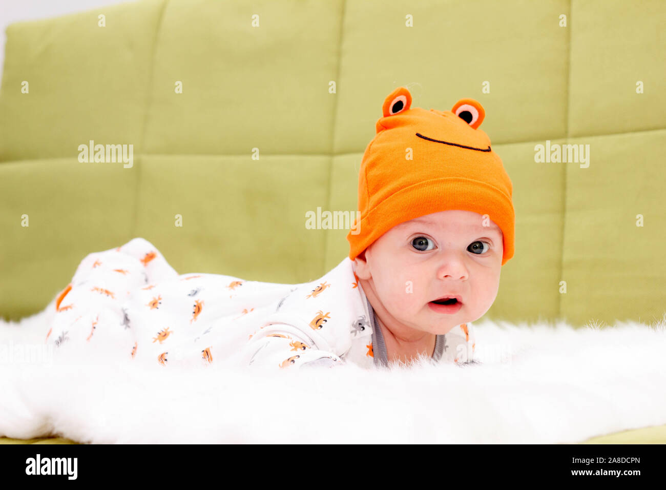 The charming Baby in an orange hat lies on a stomach on white fur Stock Photo