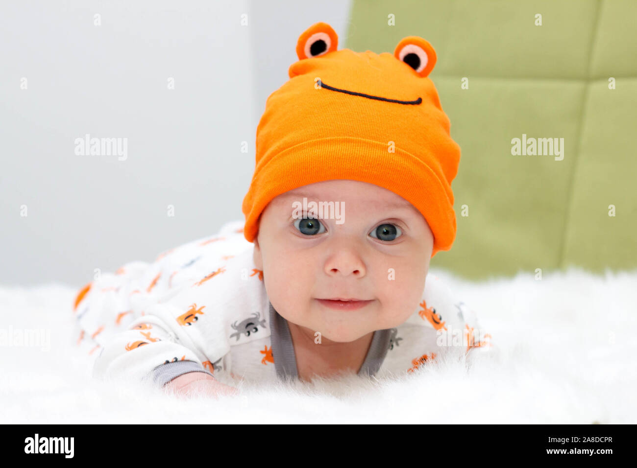 The charming Baby in an orange hat lies on a stomach on white fur Stock Photo